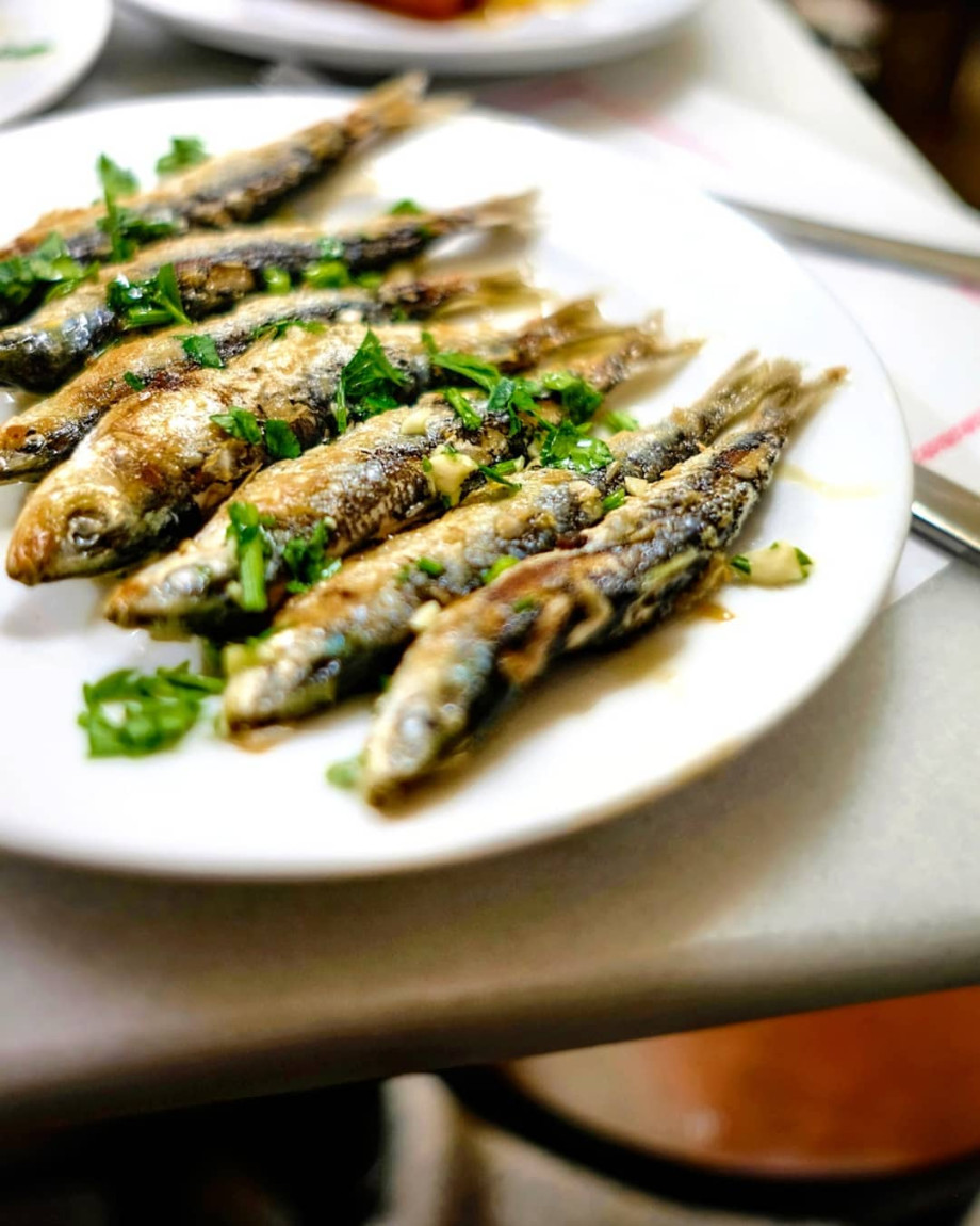 Freshly fried sardines on a plate, sprinkled with parsley.